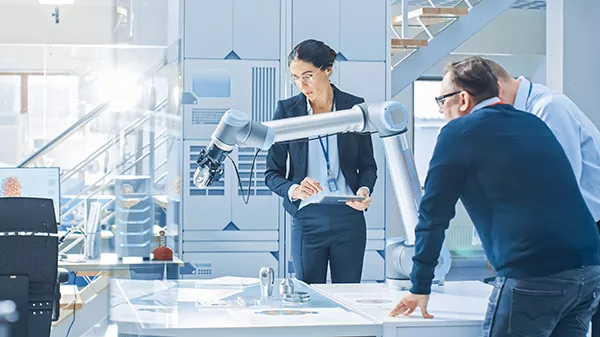 Three people in the workplace working around a robotic arm.