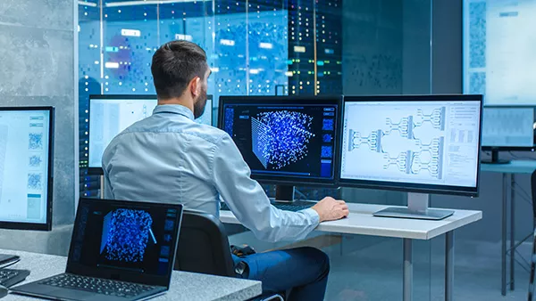 Young man in front of two computers in a professional setting.