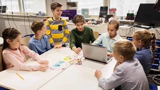 Kids at a table working on a technology project using a laptop