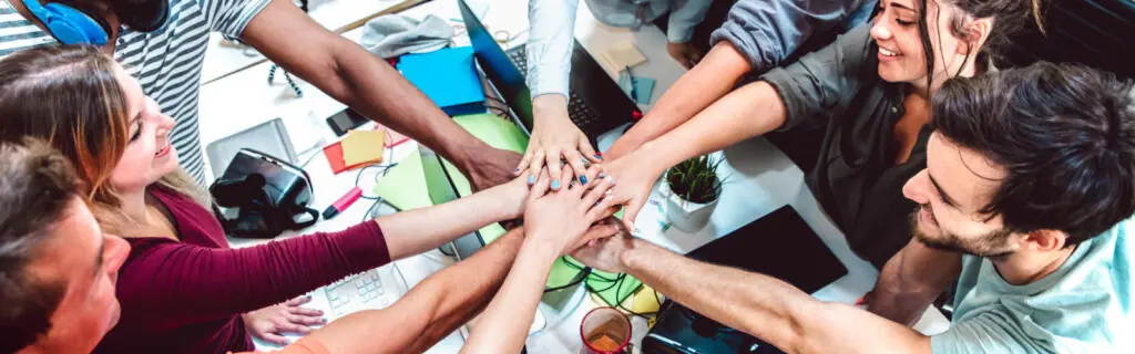 A team of adults put their hands together over a table.