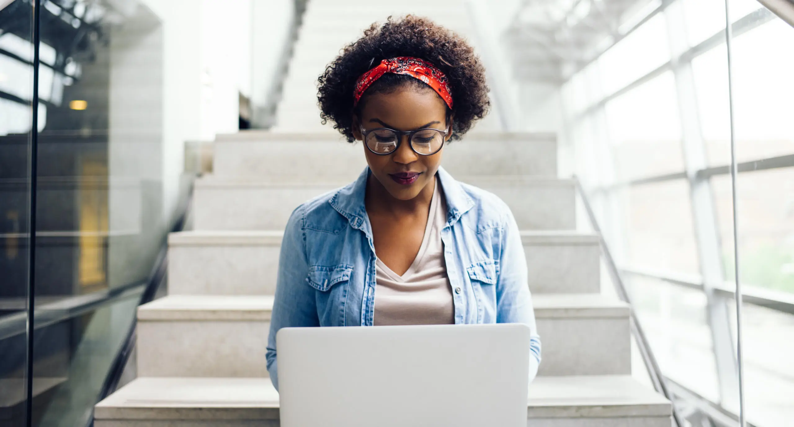 Female student working on a laptop while sitting on stairs.