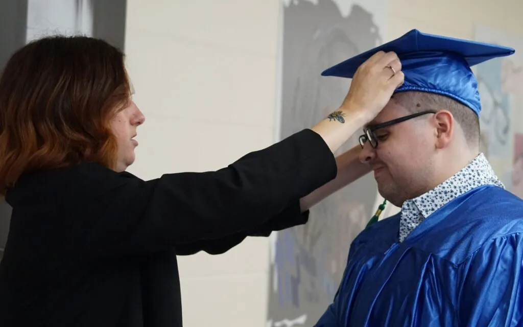 Graduate Nicolas Pinero Mortarboards getting his cap adjusted by a woman at graduation.