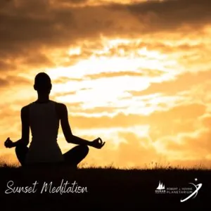 A silhouette of a person meditating on grass at sunset with a bright orange sky.