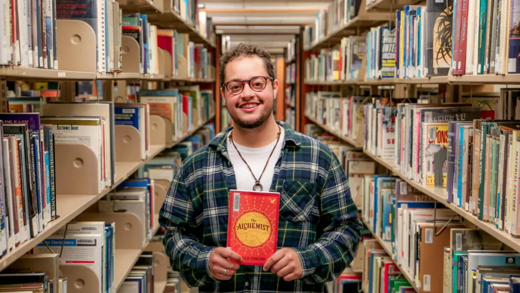 Male student in library displaying a book
