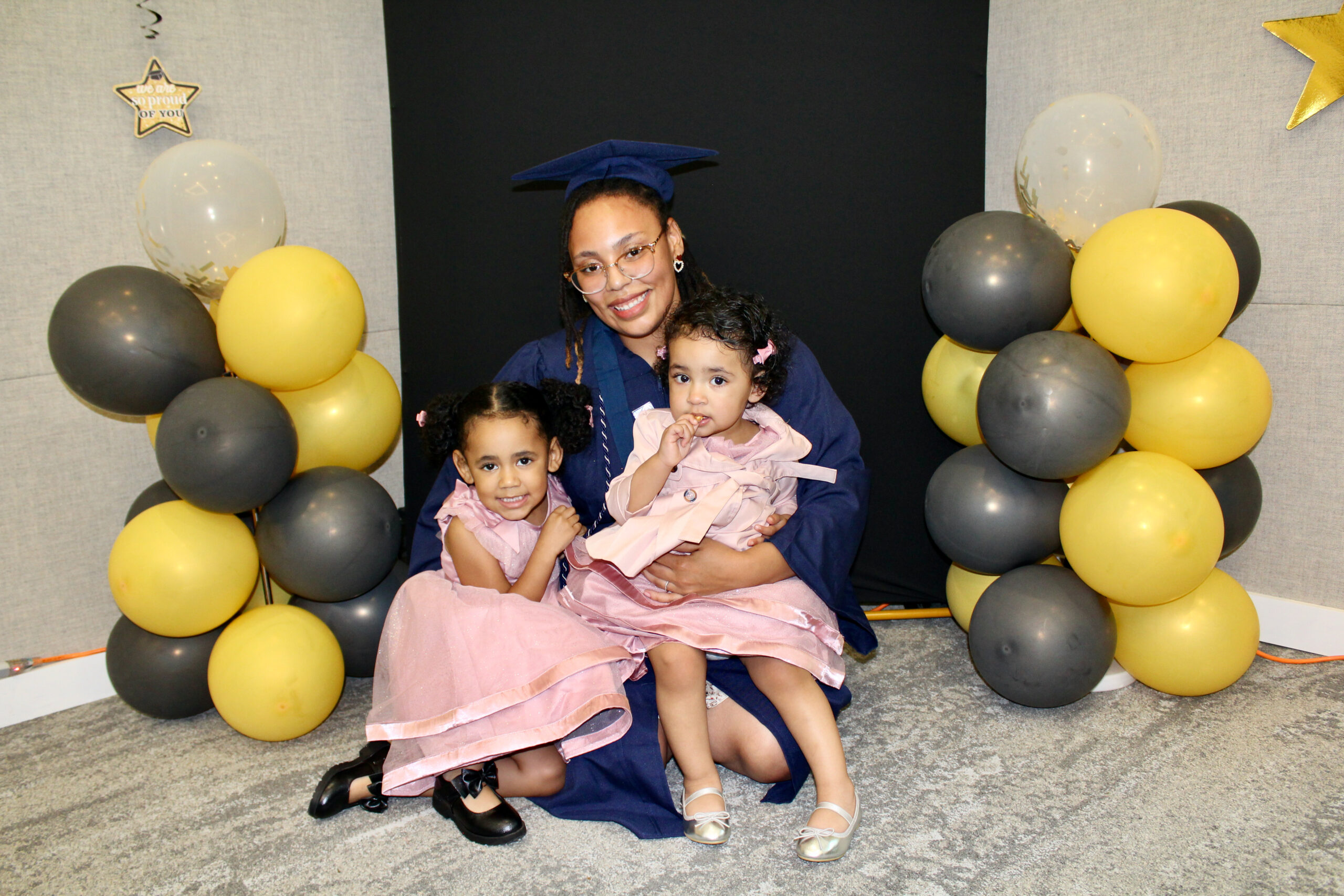 A student posing with her two young children in graduation regalia