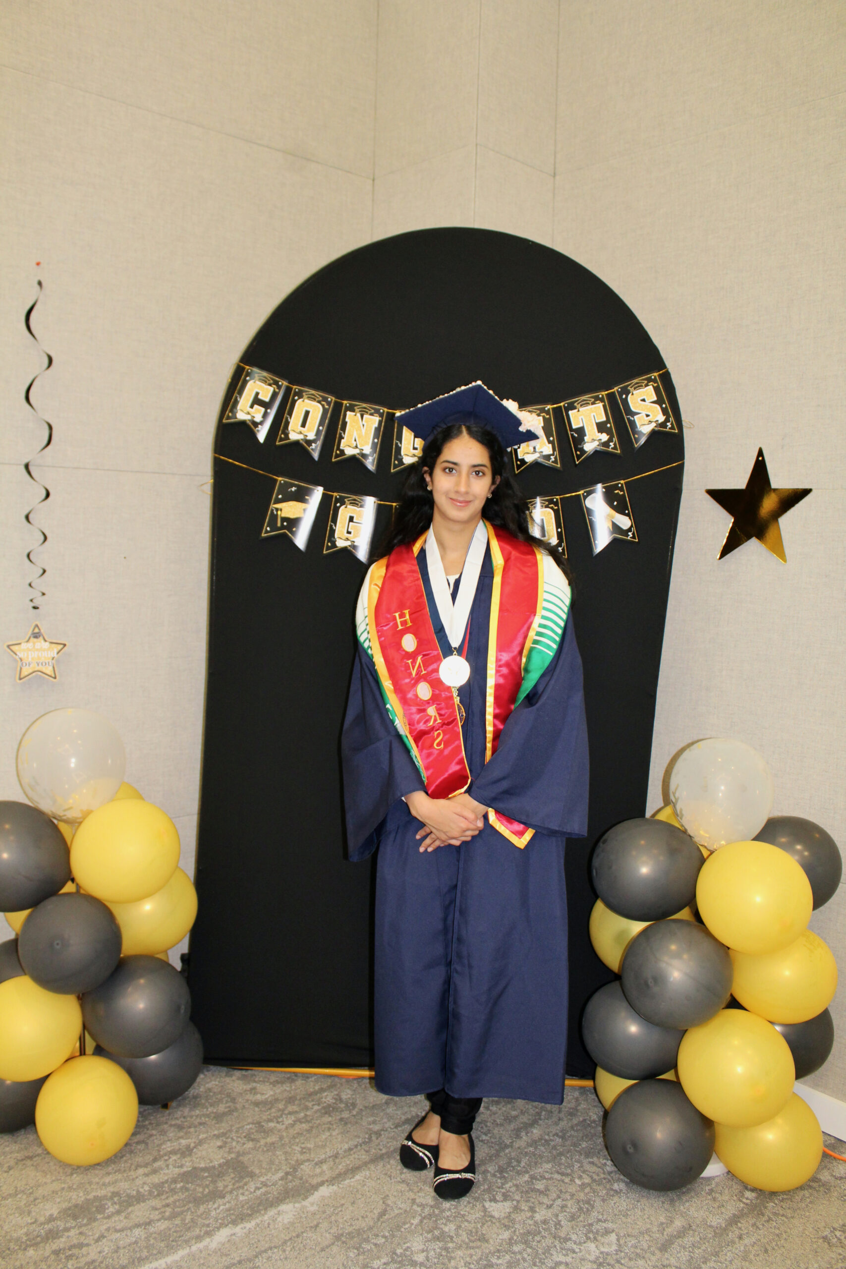 Student in graduation regalia standing in front of a photo backdrop