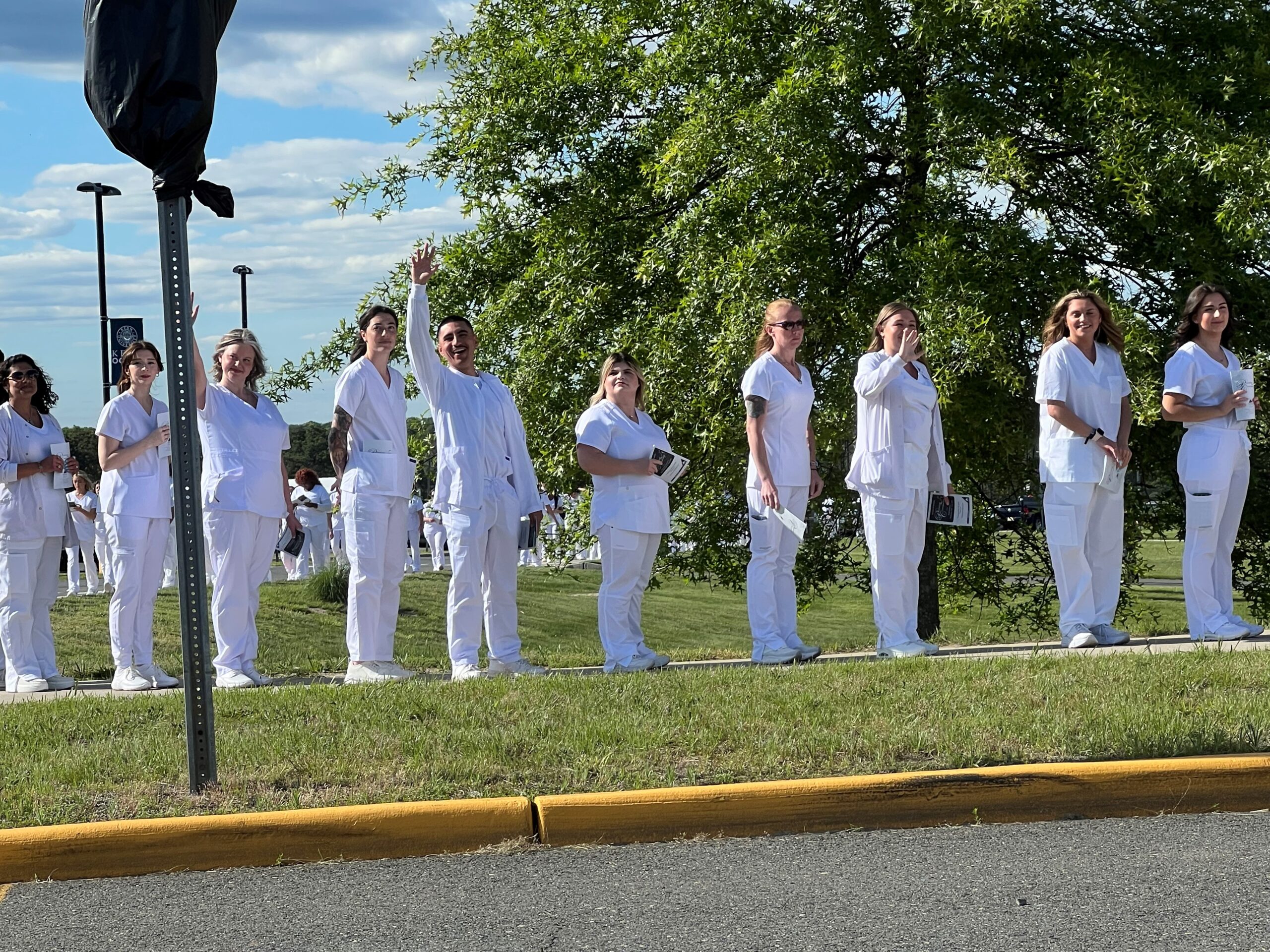 EOF student standing in a student line at the nursing pinning ceremony waving at the camera