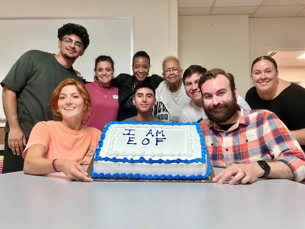 group of students and staff posing with a cake that says "I am EOF"