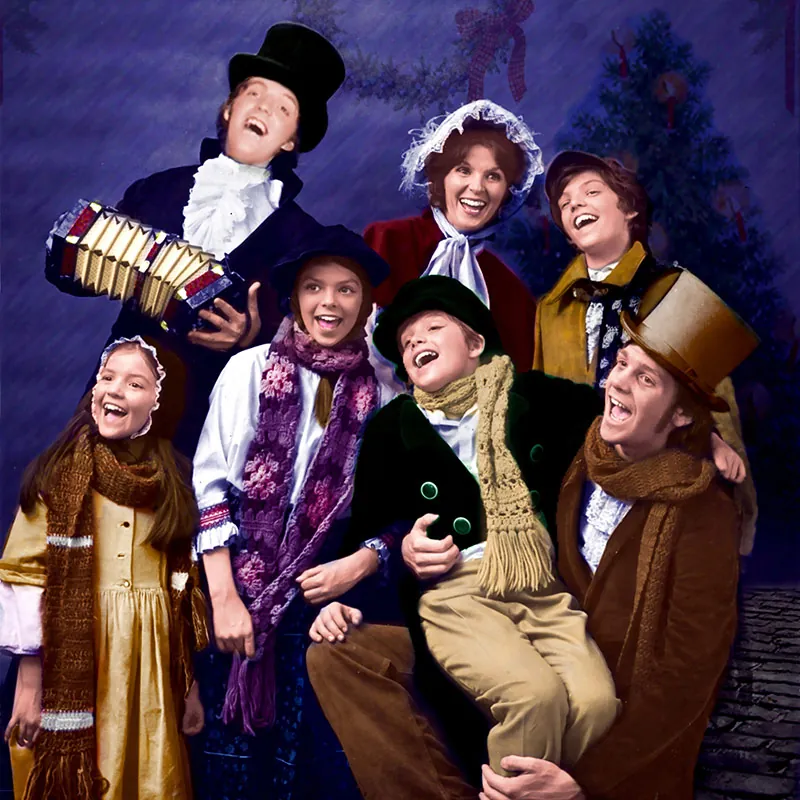 A group of people in Victorian-era winter clothing, smiling together in a festive setting.