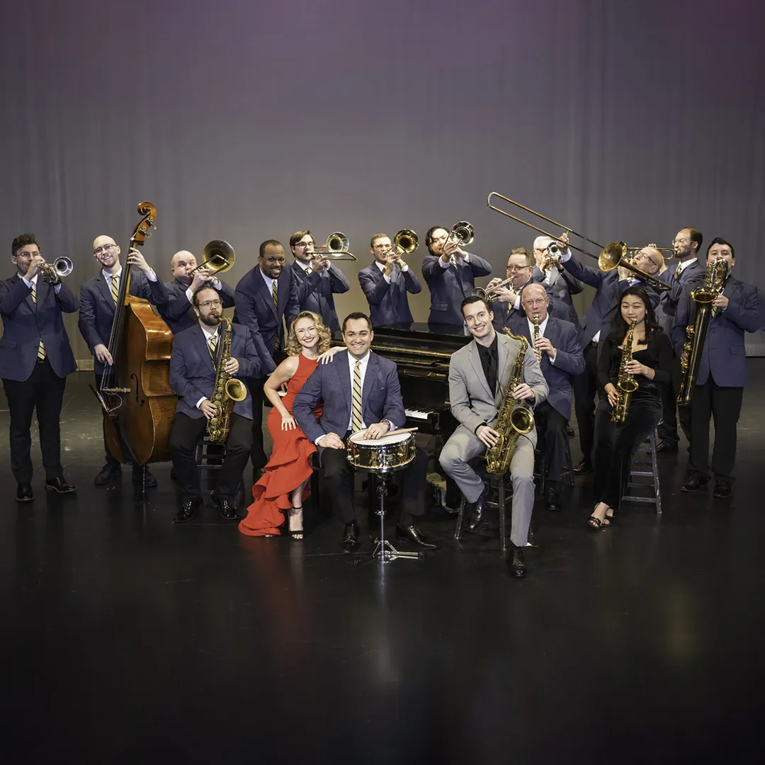 A jazz band with fifteen musicians on stage, wearing formal attire with various instruments including trumpets, trombones, saxophones, and a double bass.
