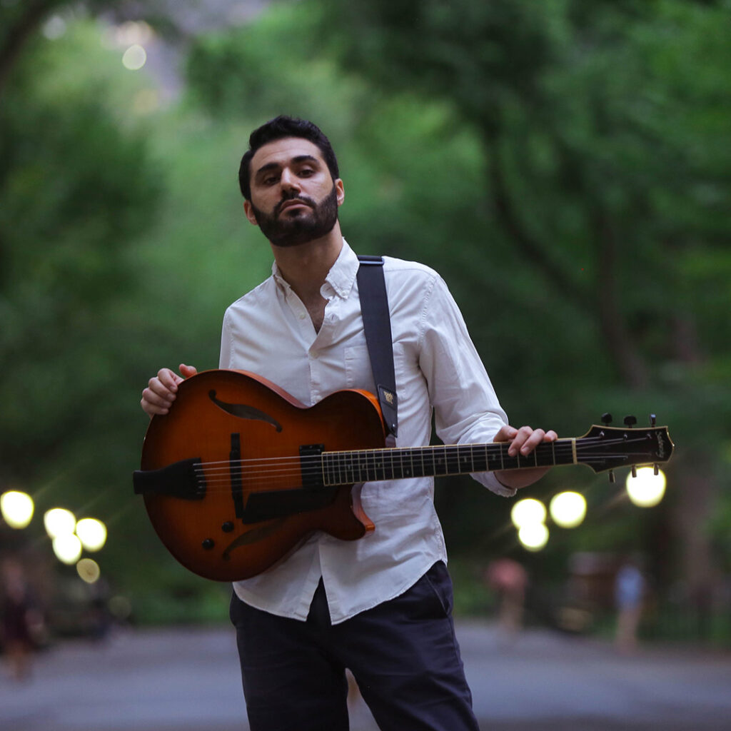 Person in a park holding a semi-hollow electric guitar.