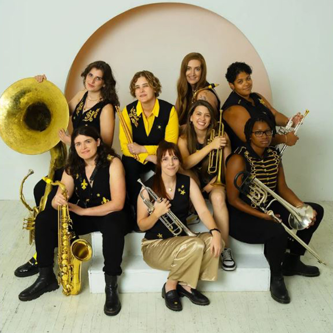 A group of eight people in coordinated black and gold outfits, holding various brass instruments,