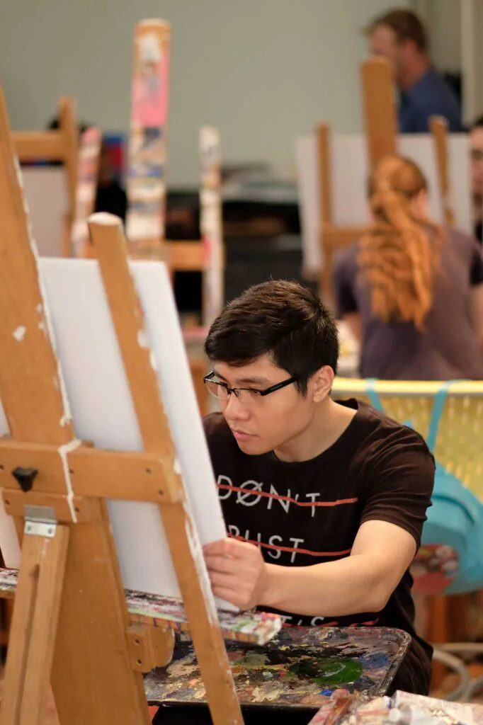 male student in art studio working on a canvas propped on an art easel