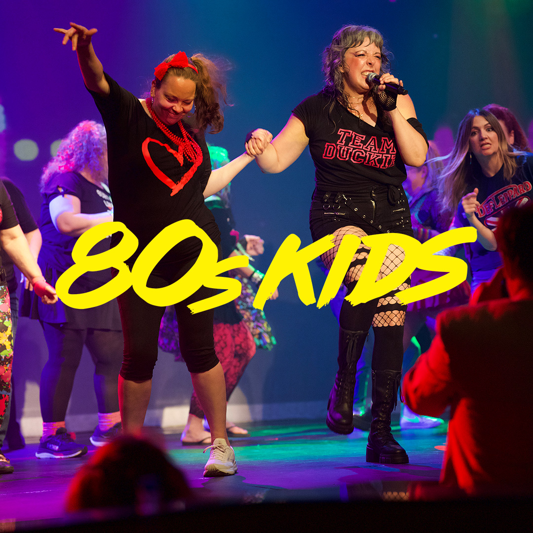 Two female performers on a brightly lit stage holding hands and dancing, with a large yellow '80s KIDS' logo across the foreground.