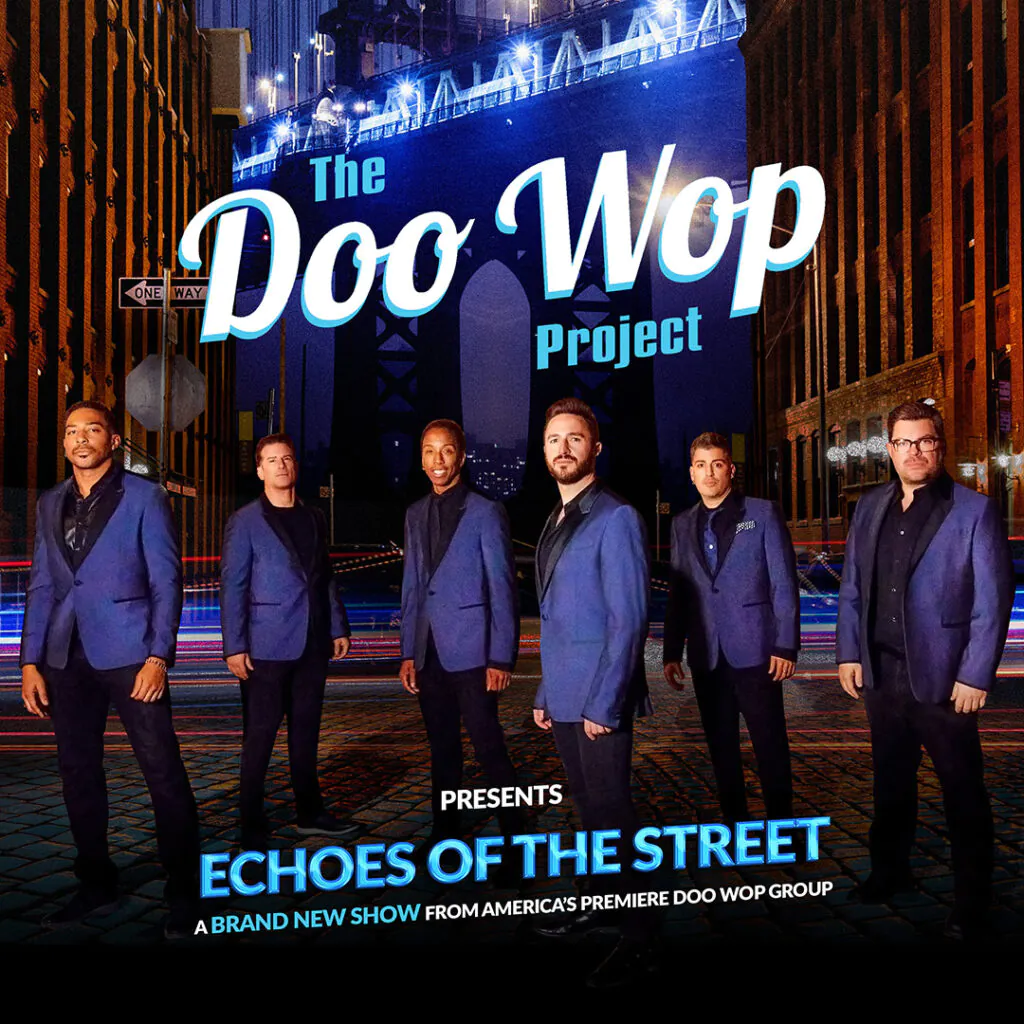 Six men in blue suits on a cobblestone street with streaks of light and surrounding buildings at night.