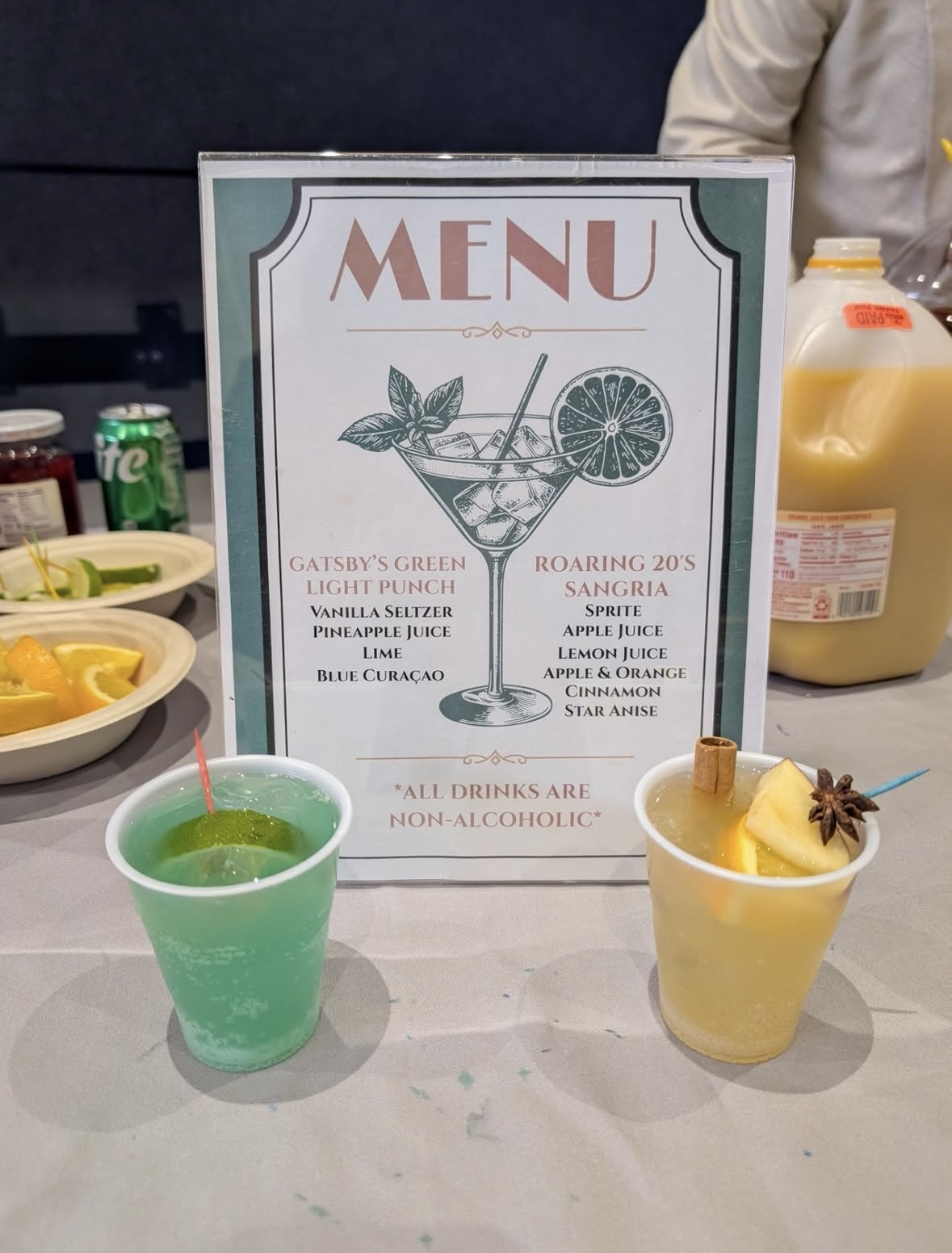 Menu board with a cocktail illustration; two cups with green and yellow non-alcoholic drinks on a table.