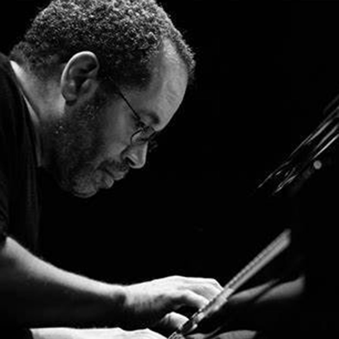 A black and white photo of a man in glasses playing piano